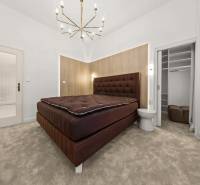  EXKLUZÍVNY, VEĽKOMETRÁŽNY 3i byt ( 130 m2 ), REKONŠTRUKCIA, CENTRUM - Spálňa so svetlým kobercom, čalúnenou posteľou a vstupom do šatníka v 3-izbovom byte.