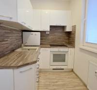 MODERNÝ 2i byt, REKONŠTRUKCIA, KLÍMA, MOZARTOVA ulica, Horský park - Kuchyňa v 2-izbovom byte, biele skrinky, podlaha s dreveným dekorom, žalúzie na oknách.