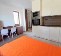 PEKNÁ GARSÓNKA, NOVOSTAVBA, KLÍMA, DRAŽDIAK HAUS, Antolská ulica - Garsónka s kuchyňou, stôl so stoličkami, posteľ a podlaha s dreveným dekorom.