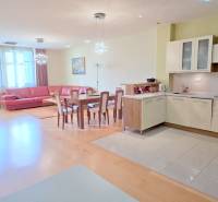 VEĽKOMETRÁŽNY 3i byt, 3 x NEPRIECHODNÁ IZBA, KLÍMA, BALKÓN, Nám.SNP - Obývacia izba v 3-izbovom byte s podlahou s dreveným dekorom, kuchyňou a červenou sedačkou.