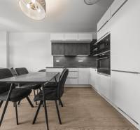 ŠTÝLOVÝ 2i byt,SKY PARK,VÝHĽAD,LOGGIA,PARKING,VEŽA II,Továrenská ul. - Kuchyňa v 2-izbovom byte s jedálenským stolom, čiernymi stoličkami a podlahou s dreveným dekorom.