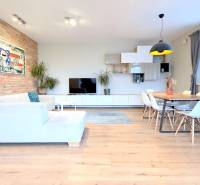 LUXUSNÝ 3i byt, TERASA, PARKING, KLÍMA, ZELENÁ HORKA, Ďumbierska ulica - Obývačka s bielym nábytkom, podlaha s dreveným dekorom, tehlová stena, obraz bankovky.