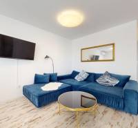 4-izbový byt 92m2 + terasa 14m2 | Bernolákovo - Modrá sedačka, zrkadlo a televízor v 4-izbovom byte s podlahou s dreveným dekorom.