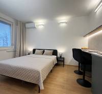 Bez provízie | Na prenájom dizajnové štúdio v Ružinove - Garsónka s posteľou, stolom a podlahou s dreveným dekorom, klíma na stene.