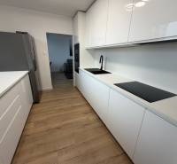 3 izbový byt s balkónom Topoľčany / PRENAJOM  - Kuchyňa v 3-izbovom byte s podlahou s dreveným dekorom a bielymi skrinkami.