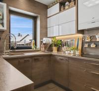 Ideálny dom pre rodinu, Blatné, okr. Senec - Kuchyňa v rodinnom dome s podlahou s dreveným dekorom, rastliny a poličky s čajovými súpravami.