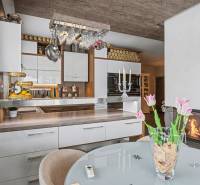 Ideálny dom pre rodinu, Blatné, okr. Senec - Kuchyňa s bielymi skrinkami, barovým pultom a skleneným stolom s kvetmi v rodinnom dome.