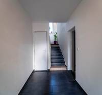 ATRAKTÍVNY 2 IZBOVÝ BYT S VLASTNOU ZÁHRADKOU a 3 parkovacími miestami - Chodba s tmavou dlažbou a schodmi, vedie k dverám s kvetinou na poschodí.