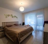 ATRAKTÍVNY 2 IZBOVÝ BYT S VLASTNOU ZÁHRADKOU a 3 parkovacími miestami - Spálňa 2-izbového bytu s posteľou, dekorom na stene a presklenými dverami.