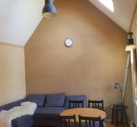 Na predaj záhradná chatka - Chata so šikmým stropom, sedačkou, okrúhlym stolom a podlahou s dreveným dekorom.