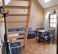 Na predaj záhradná chatka - Interiér chaty s podlahou s dreveným dekorom, sedačkou, schodmi a stolom so stoličkami.