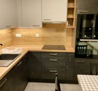 I Prenájom moderne zariadeného 3-izbového bytu v Petržalke. - Kuchynská linka v 3-izbovom byte s drevenými dekormi, čiernym drezom a zabudovanými spotrebičmi.