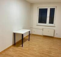 I Prenájom moderne zariadeného 3-izbového bytu v Petržalke. - Prázdna izba s bielym stolom a podlahou s dreveným dekorom v 3-izbovom byte.