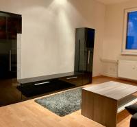 I Prenájom moderne zariadeného 3-izbového bytu v Petržalke. - Obývacia izba v 3-izbovom byte s čiernou obývačkovou stenou a podlahou s dreveným dekorom.