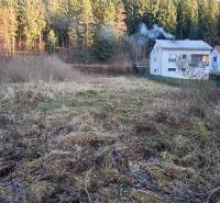 Stavebný pozemok Svrčinovec - Pozemky na bývanie v Svrčinovci, lúka s domami a lesom v pozadí.