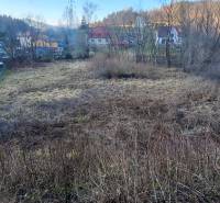 Stavebný pozemok Svrčinovec - Pozemok na bývanie v Svrčinovci obklopený stromami a blízke domy v pozadí.