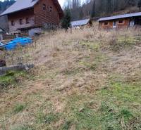 Lukratívny stavebný pozemok - Pozemok v Oščadnici určený na bývanie s viditeľnými drevenými stavbami na svahovitom teréne.