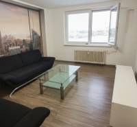 Na predaj: 2-izbový byt v centre mesta Galanta – časť Nová Doba - Obývačka v 2-izbovom byte s čiernym gaučom, skleneným stolom a podlahou s dreveným dekorom.