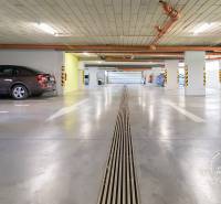 ŠPIČKOVO KOMPLETNE ZARIADENÝ 2-izb. byt bez kompromisov - Podzemná garáž s parkovacími miestami, šedá podlaha, osvetlené priestory, autá zaparkované.