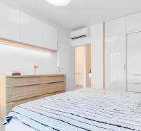 ŠPIČKOVO KOMPLETNE ZARIADENÝ 2-izb. byt bez kompromisov - Spálňa v 2-izbovom byte s bielymi skriňami a dreveným dekorom komody.