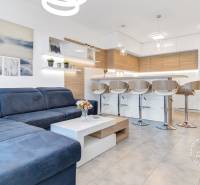 ŠPIČKOVO KOMPLETNE ZARIADENÝ 2-izb. byt bez kompromisov - Obývacia izba v 2-izbovom byte s bielou kuchyňou a barovými stoličkami.