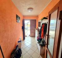 5.izb RD Čereňany pozemok 1028m - Chodba v rodinnom dome s oranžovými stenami a dlažbou, plná kabátov a obuvi.