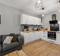 I Na predaj priestranný 2-izbový byt v Rovinke (City Park) - Kuchyňa v 2-izbovom byte s bielou linkou, sivou sedačkou a podlahou s dreveným dekorom.