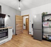 I Na predaj priestranný 2-izbový byt v Rovinke (City Park) - Kuchyňa 2-izbového bytu s podlahou s dreveným dekorom, chladničkou a policovými regálmi.