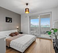 I Na predaj priestranný 2-izbový byt v Rovinke (City Park) - Spálňa v 2-izbovom byte s posteľou, podlaha s dreveným dekorom, balkónové dvere.