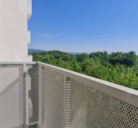 Zariadený 2-izb. byt v novostavbe v Ružinove - Ovocné sady - Balkón s výhľadom na les a kopce, budova v pozadí, jasná obloha.