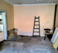 Rodinný dom Svätý Jur, centrum, pôvodný stav - Miestnosť v rodinnom dome s rebríkom, stoličkou a materiálmi na podlahe s dreveným dekorom.