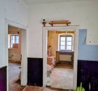 Rodinný dom Svätý Jur, centrum, pôvodný stav - Interiér rodinného domu s dreveným dekorom a starším zariadením, biele steny, okná.