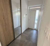 Novostavba rodinný dom Ludanice / REZERVOVANE - Vstupná chodba rodinného domu s bielymi stenami a skriňou v dekore dreva.