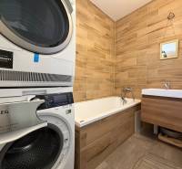Novostavba rodinný dom Ludanice / REZERVOVANE - Kúpeľňa v rodinnom dome s vaňou, práčkou a podlahou s dreveným dekorom.