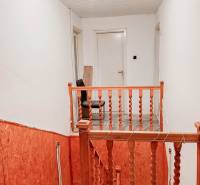 Rodinný dom, Maďarsko, obec Vizsoly - Schodisko s dreveným zábradlím v rodinnom dome, biele steny, osvetlenie so žiarovkou.