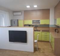 Na prenájom klimatizovaný 2 izbový byt v Moste pri Bratislave - Kuchyňa v 2-izbovom byte s podlahou s dreveným dekorom a zelenými skrinkami.