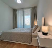 NUERA︱SKY PARK Moderný 2-izbový byt na 6. poschodí, veža 3 - Spálňa v 2-izbovom byte s posteľou, nočným stolíkom a podlahou s dreveným dekorom.