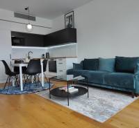 NUERA︱SKY PARK Moderný 2-izbový byt na 6. poschodí, veža 3 - Obývačka s kuchynským kútom, tyrkysovou sedačkou, dreveným dekorom a jedálenským stolom.