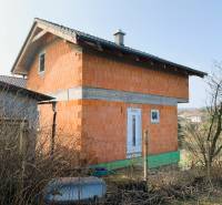 CHATA UZAVRETÁ HRUBÁ STAVBA, KOŠICKÁ NOVÁ VES - GEDER - Chata v výstavbe s tehlovými stenami pri dedine a záhrady na pozadí.