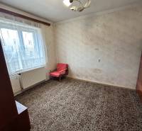 Predaj staršieho RD vo Dvoroch nad Žitavou - Izba v rodinnom dome s kobercovou podlahou, jednoduchým kreslom a závesmi.