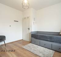 Rezervované 3-izbový byt so záhradou, Šamorín - Izba v 3-izbovom byte s posteľou, šedým kreslom a podlahou s dreveným dekorom.