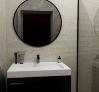 NA PREDAJ 3-IZBOVÝ RD (ČASŤ DVOJDOMU), ZEMIANSKA OLČA - Kúpeľňa v rodinnom dome s okrúhlym zrkadlom a tmavým umývadlom na bielom podklade.