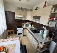 Nadštandardný 4-izbový tehlový byt po kompletnej Sahy - Kuchyňa v 4-izbovom byte s linkou, sporákom, drevenými skrinkami a okrúhlym stolom.