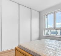 2-izbový byt, NOVÝ, veľkorysý ÚLOŽNÝ PRIESTOR, PARKOVANIE - Spálňa v 2-izbovom byte s podlahou s dreveným dekorom, veľké okno a skriňa.