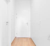 2-izbový byt, NOVÝ, veľkorysý ÚLOŽNÝ PRIESTOR, PARKOVANIE - Biela vstupná chodba so skriňou a podlahou s dreveným dekorom v 2-izbovom byte.