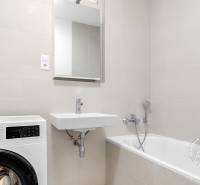 2-izbový byt, NOVÝ, veľkorysý ÚLOŽNÝ PRIESTOR, PARKOVANIE - Kúpeľňa v 2-izbovom byte s vaňou, umývadlom a práčkou v bielych odtieňoch.