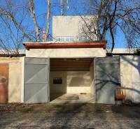 Zrekonštruovaná veľká garáž na ul. Agátova, Dúbravka s pozemkom - Garáž na Agátovej ulici v Bratislave - Dúbravke s plechovými dverami a stoličkou vonku.