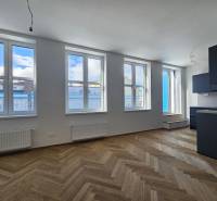 VÝNIMOČNÝ APARTMÁN priamo v centra mesta - projekt UNO Poštová - 1-izbový byt s podlahou s dreveným dekorom a čiernou kuchynskou linkou.