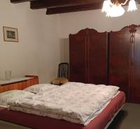 Na predaj RD na bývanie alebo investičná príležitosť Horné Saliby - Spálňa v rodinnom dome s dreveným stropom, starožitnou skriňou a klasickým lustrom.