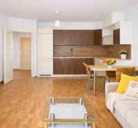 INVESTIČNÉ BÝVANIE V TOP LOKALITE: 2-IZBOVÝ BYT, JÉGÉHO UL, BRATISLAVA - Obývačka 2-izbového bytu s kuchyňou, podlahou s dreveným dekorom a pohodlným sedením.